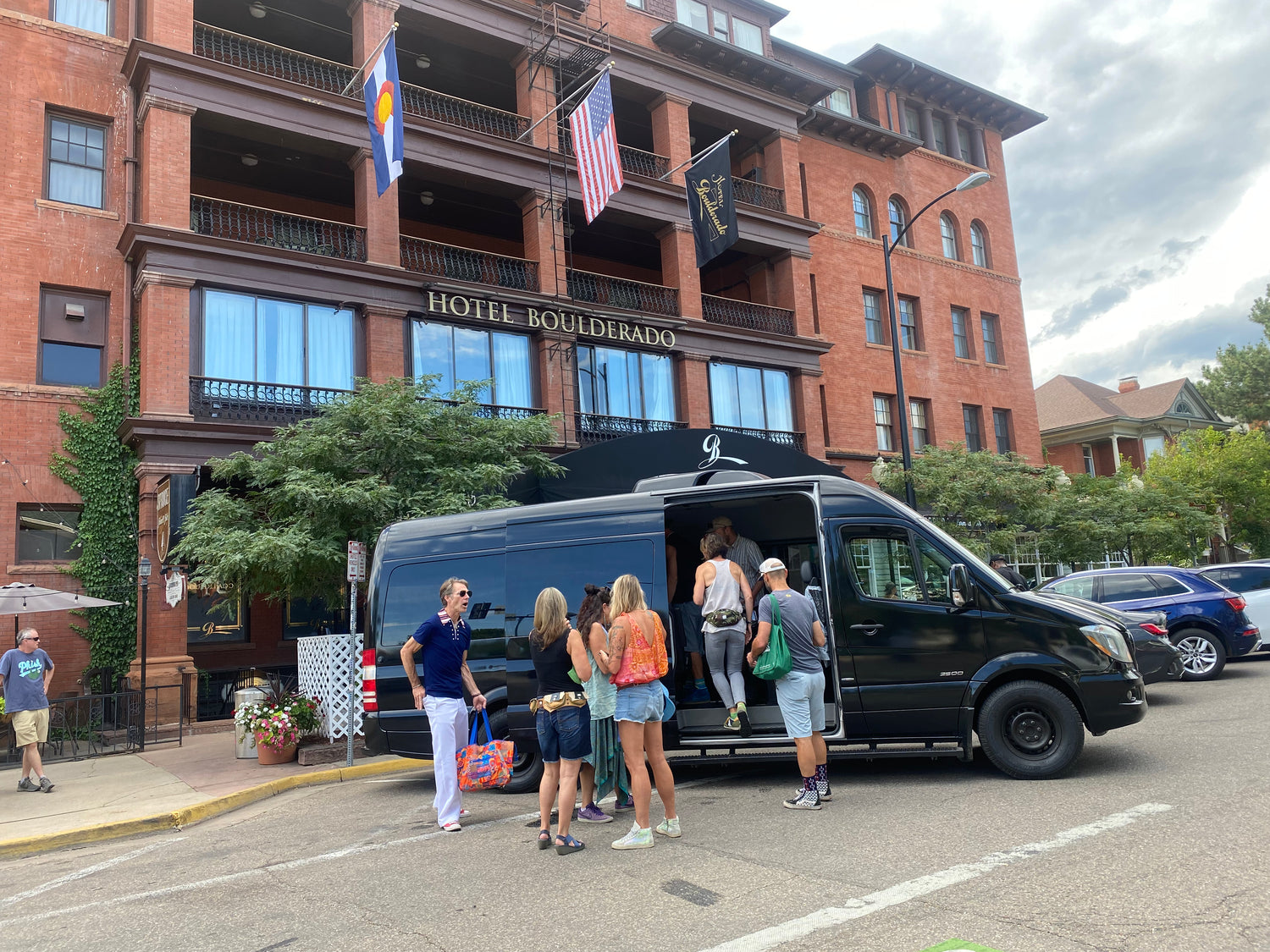 Black van with people boarding in front of a brick building labeled 'Hotel Boulderado'. ridetoredrocks.com